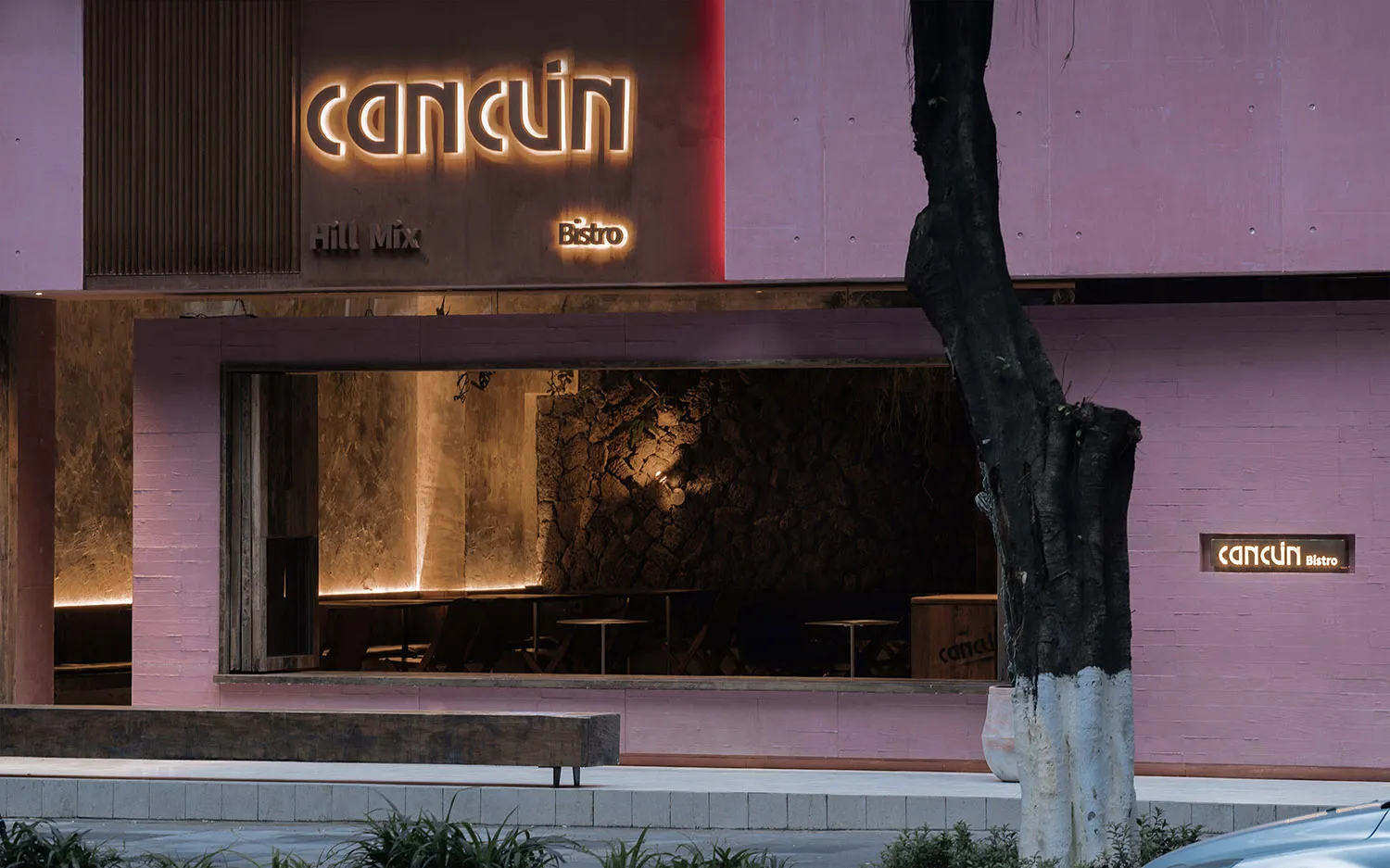 A well-lit restaurant with a pink accent wall, large windows, and comfortable seating areas with chairs and dining tables