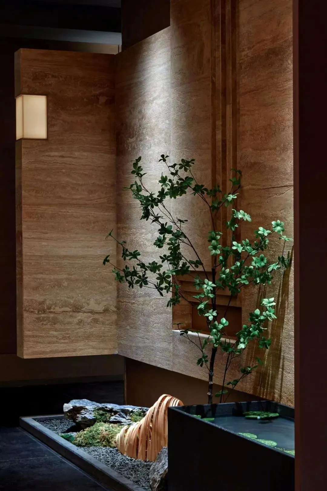 Indoor space with a stone wall, wooden bench, and two potted plants, creating a calm and inviting atmosphere