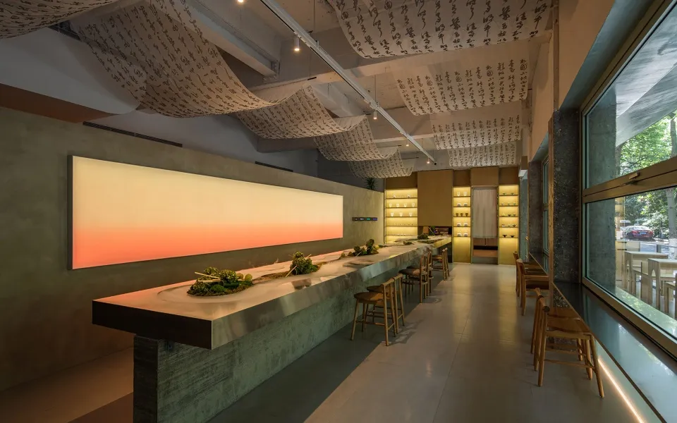 A modern Asian restaurant with a long wooden bar, oriental decorations, and multiple bowls on the counter