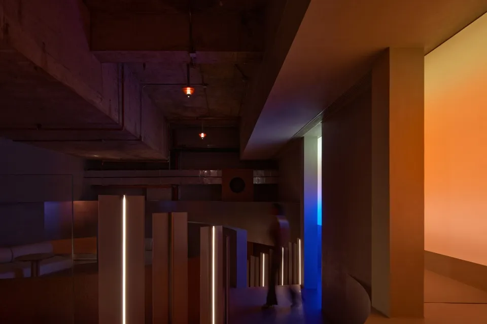A well-lit hallway in a historic building with a staircase, worn walls, and two people walking down the hall
