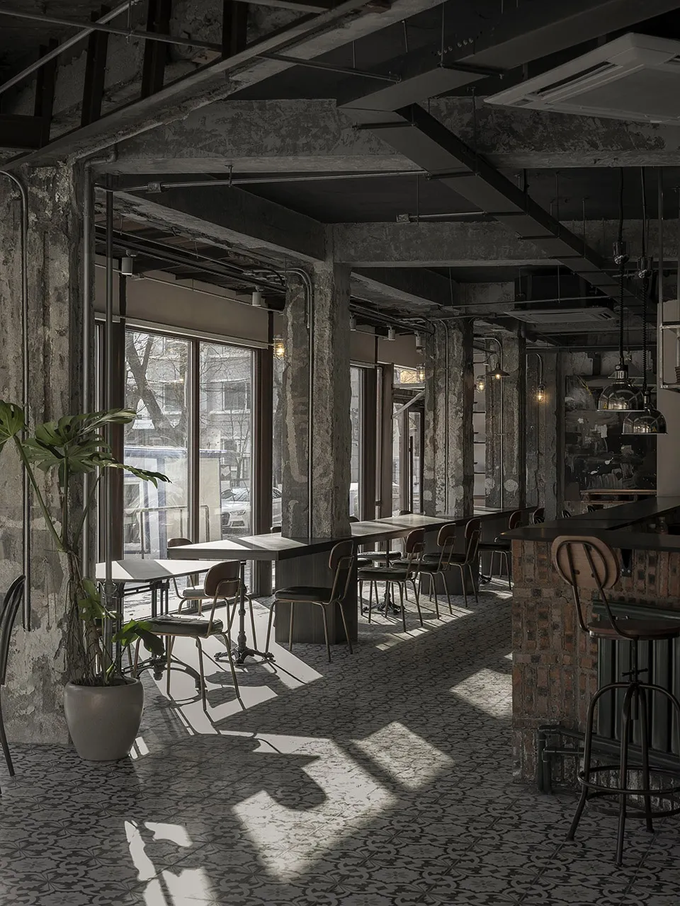 Empty restaurant interior with brick walls, dining tables, and chairs, flooded with natural light through a large window
