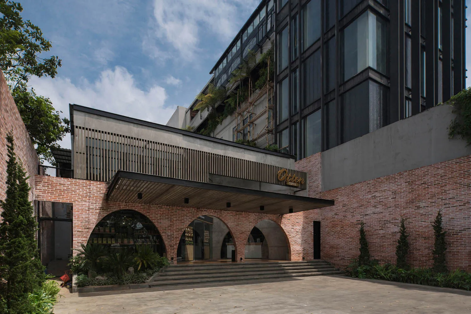 磚牆立面的現代建築，設有大型拱門、陽台及盆栽植物，配有兩張長椅，營造溫馨的氛圍
