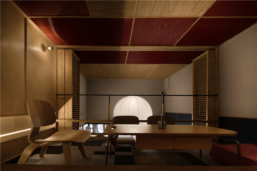 Dining area with a wooden table, two chairs, a couch, and red accent walls, set in a modern space with clean lines and minimal decoration