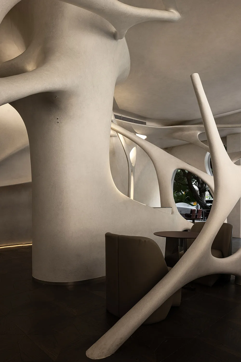 A modern living space with curved walls, a spiral staircase, and various furniture pieces, well-lit with natural and artificial light, and accented with potted plants