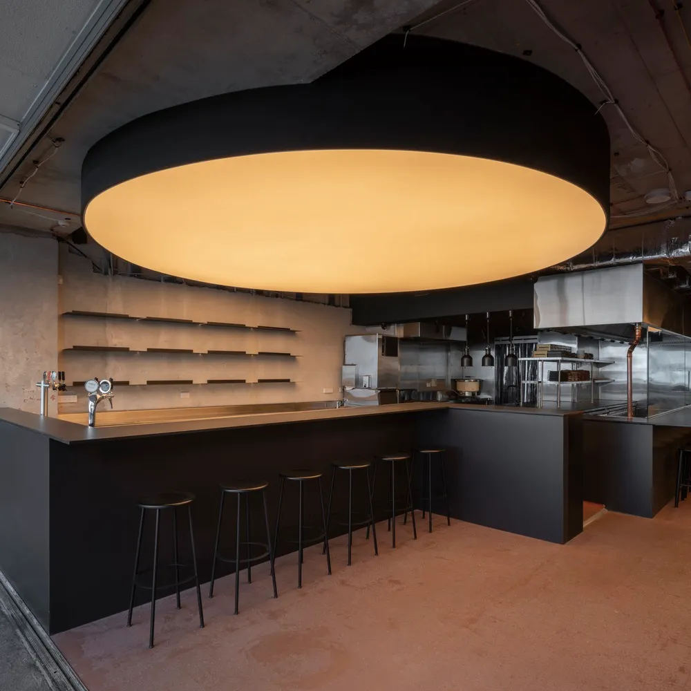 Industrial kitchen with a black dome light, counter, and stools, giving off a modern and sleek vibe