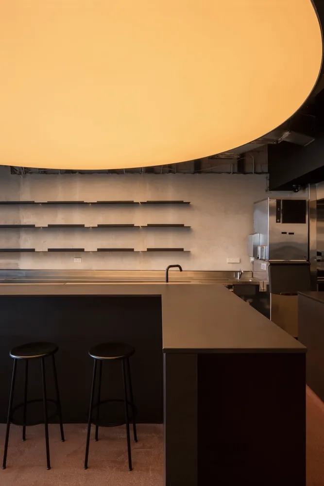 Industrial kitchen with a black countertop, stools, a refrigerator, and an oven, with a modern and functional atmosphere