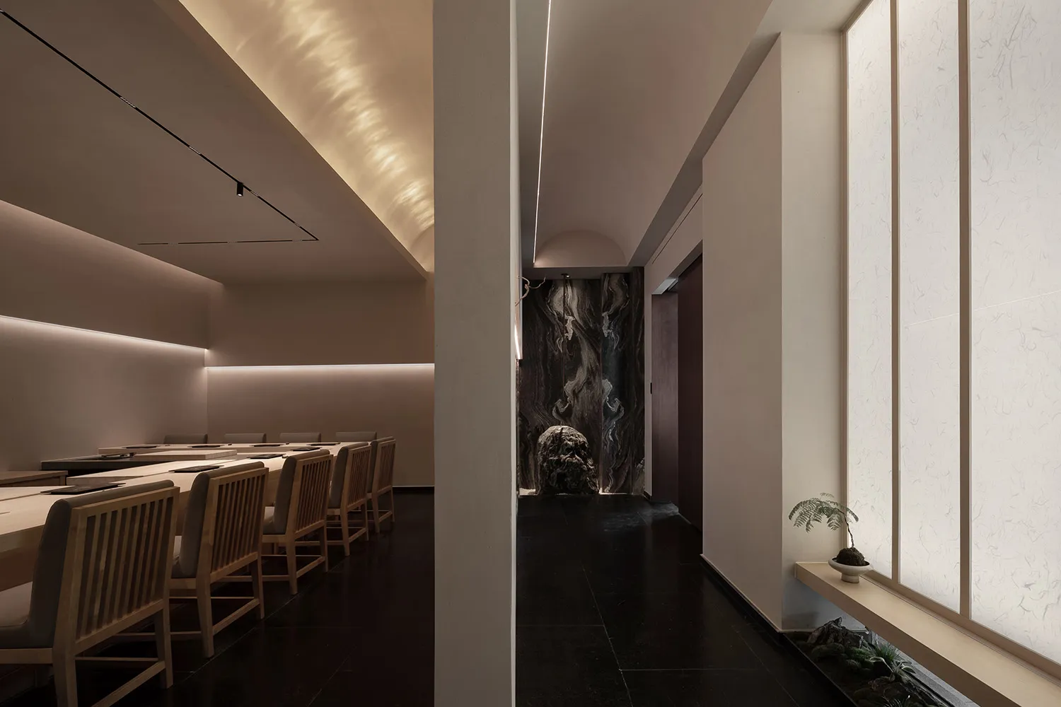 A dimly lit restaurant dining area with chairs, a dining table, and marble accents on the walls