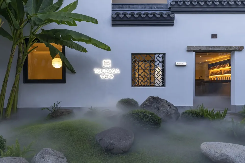 外觀潔白的亞洲風住宅，配有綠色屋頂與前方的大型磚石庭園，融合傳統與現代元素，營造寧靜而溫馨的氛圍