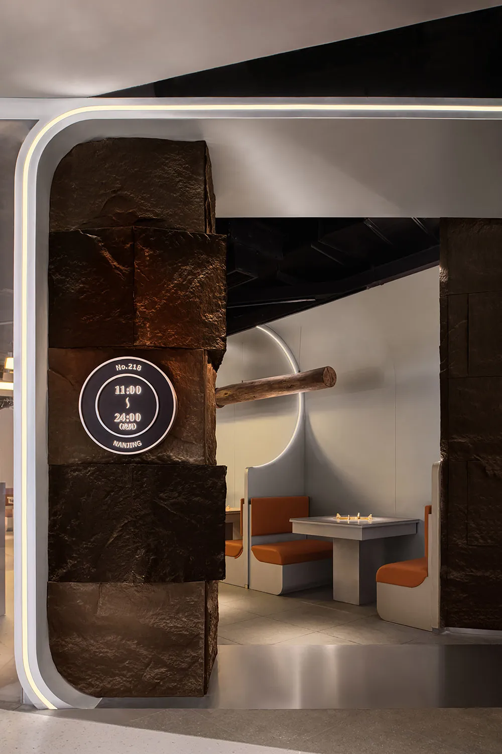 Cozy cafe interior with a stone wall, wooden elements, and two orange chairs in a dimly lit space