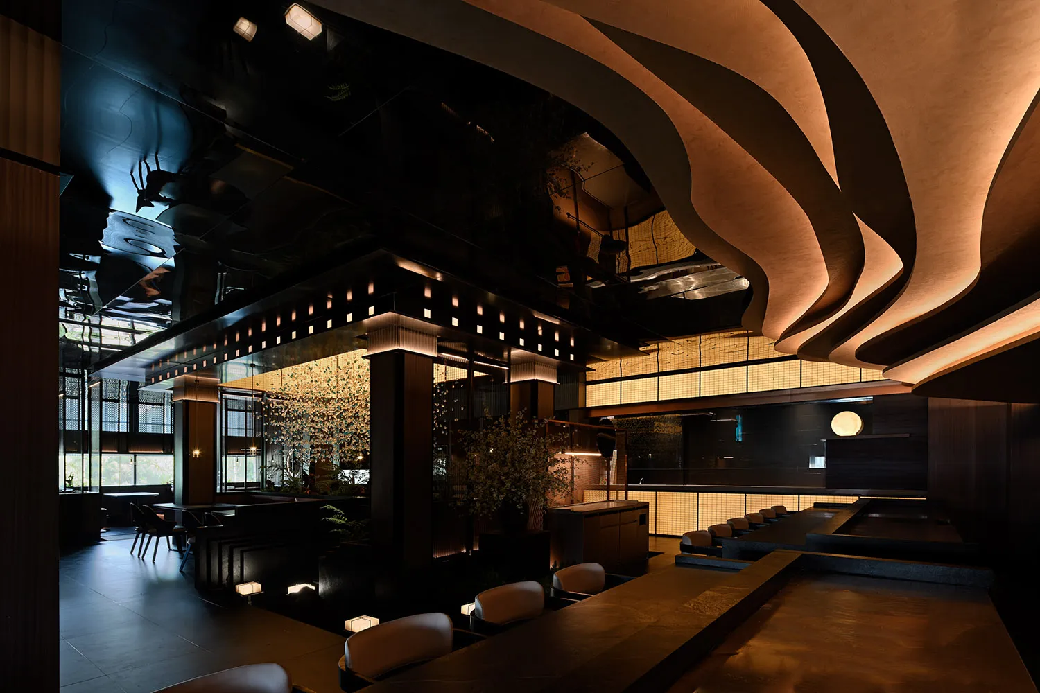 A warm and inviting restaurant interior with a large dining table, potted plants, decorative lights, vases, and artwork on the walls