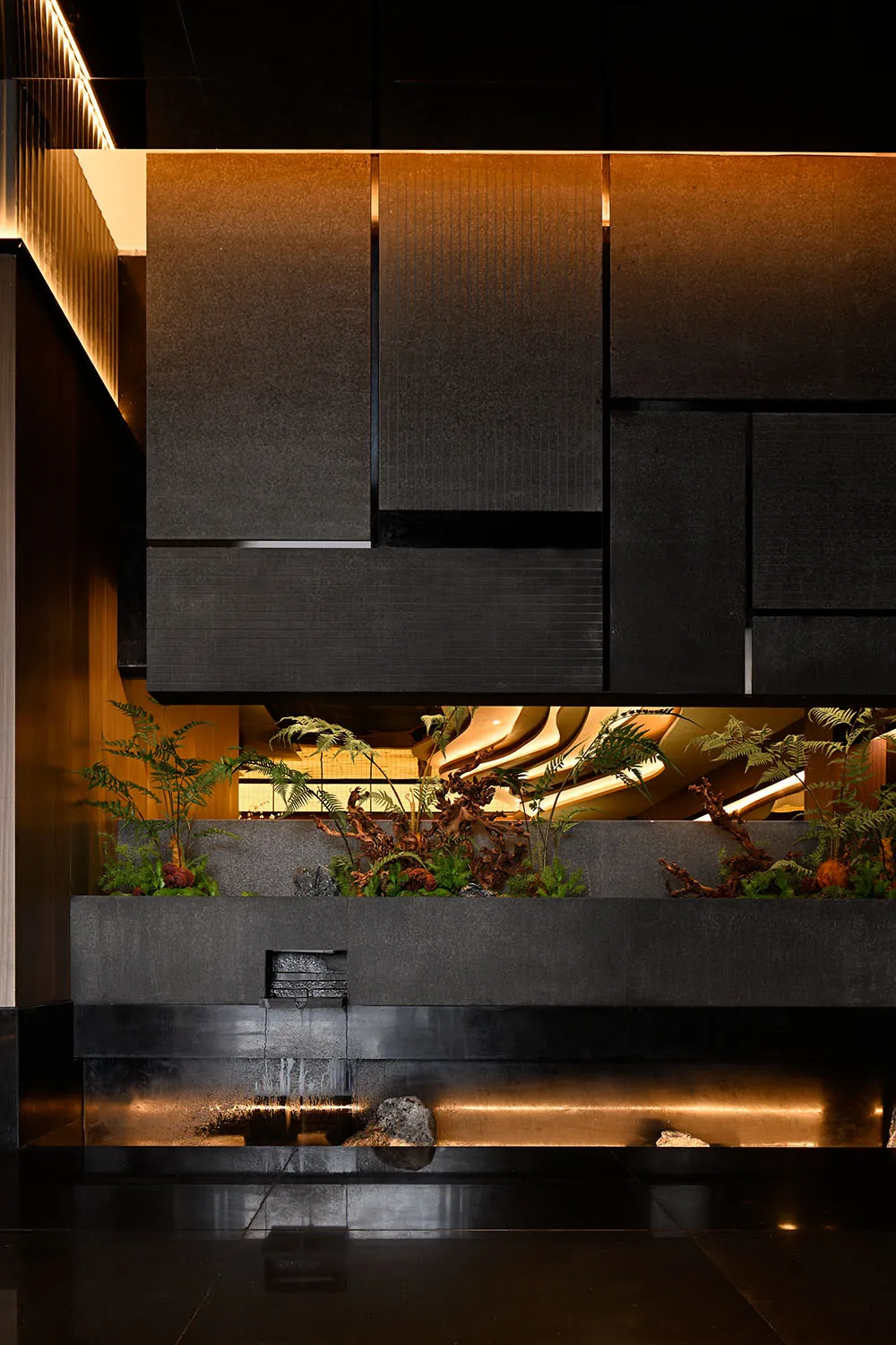 A modern bathroom with a black countertop featuring a waterfall fountain, surrounded by potted plants, creating a relaxing atmosphere