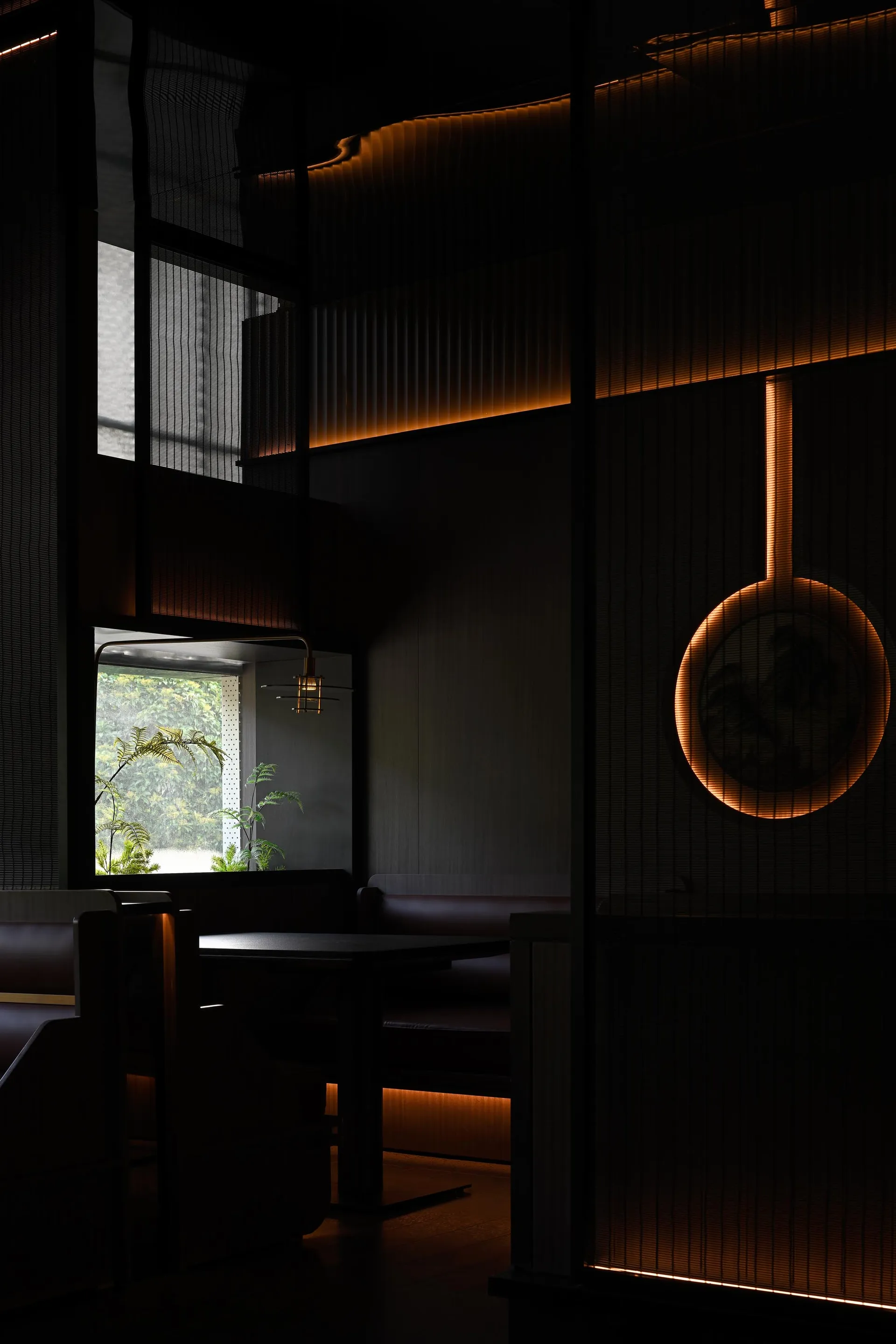 A cozy restaurant dining area with black walls, natural light, and a large table surrounded by chairs