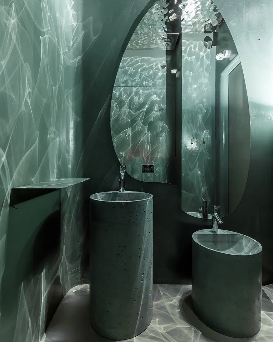 Bathroom with two concrete sinks under a mirror in a dimly lit space with a modern and minimalist aesthetic