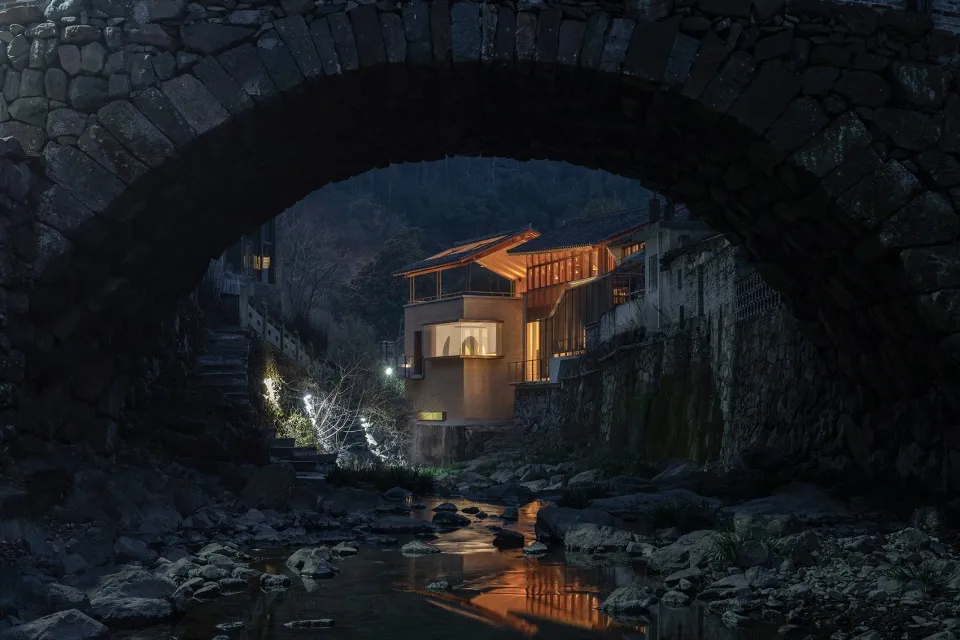 河邊石屋，寧靜氛圍，兩人站在戶外，環境祥和