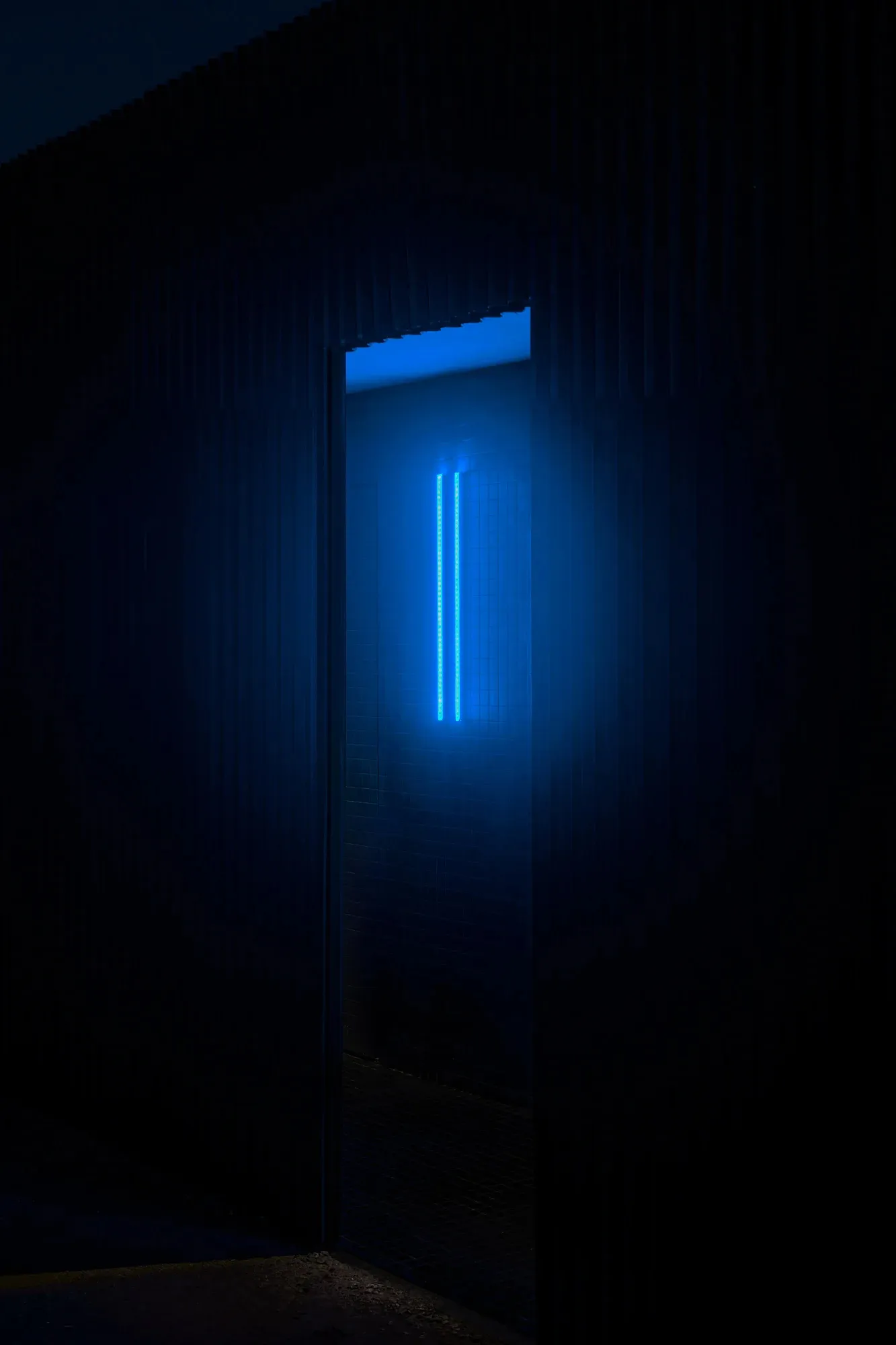 A dark room with a glass door and two lights on either side, providing illumination to the area beyond
