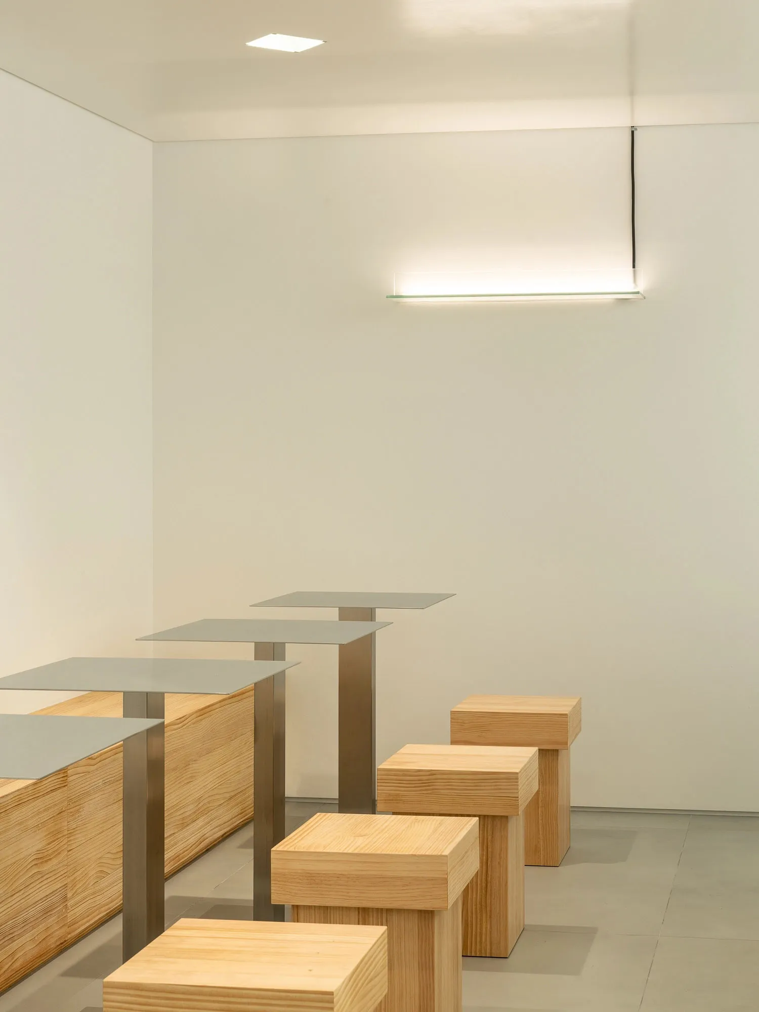 A minimalist interior design concept featuring a row of three wooden stools placed on a white wall, creating a clean and simple arrangement