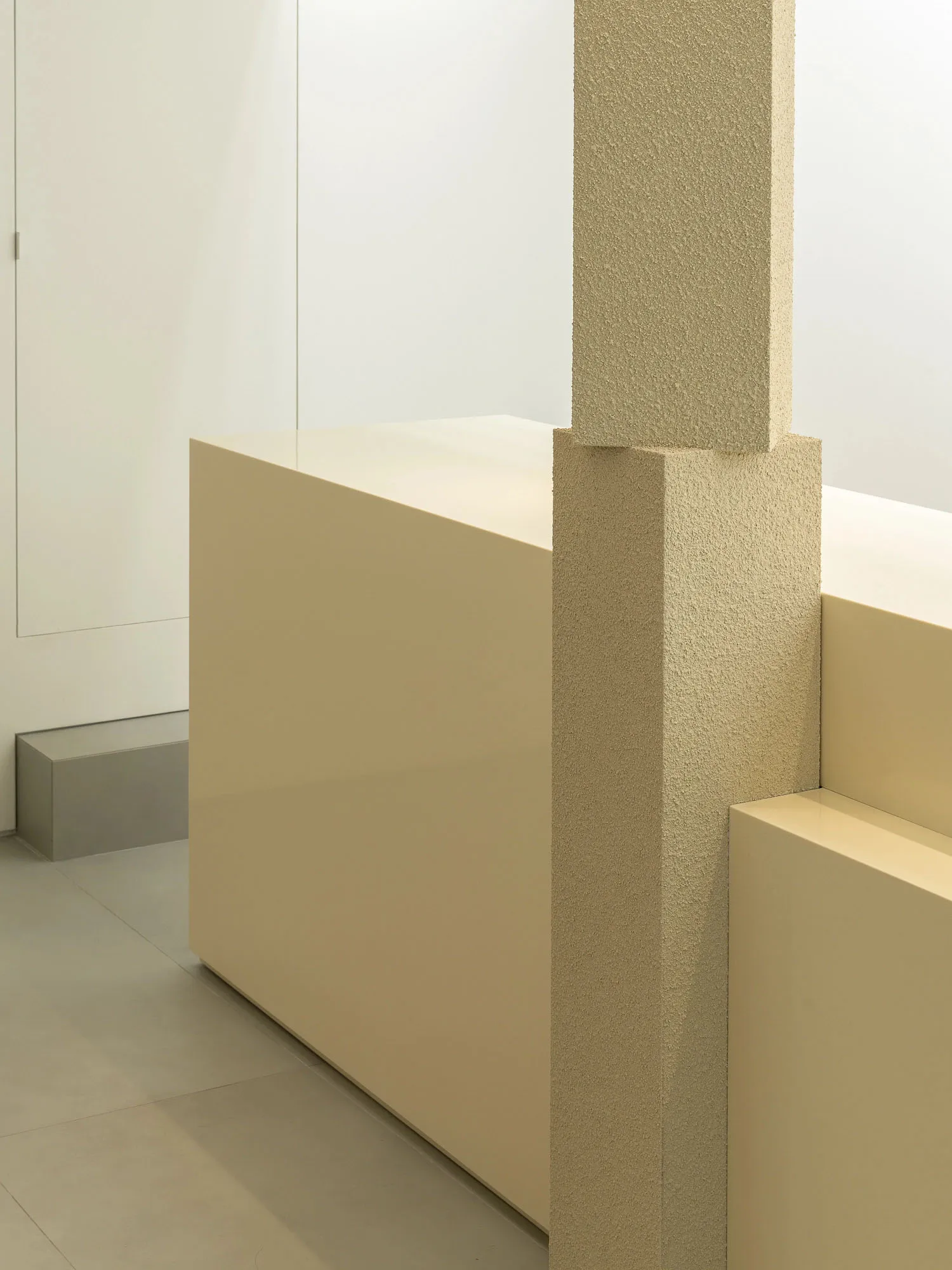 A modern interior space with a white wall, a concrete pillar, and two benches in a symmetrical arrangement, giving a clean and bright appearance