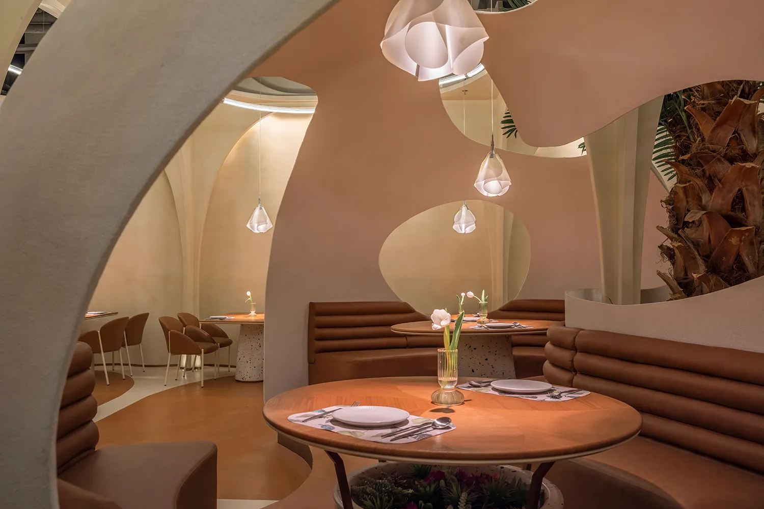 Dimly lit restaurant interior with tables, chairs, potted plants, artwork, and wood and stone materials