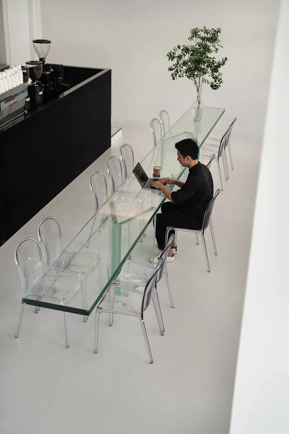 Casual dining space with a glass table, chairs, and people using a laptop and sitting nearby