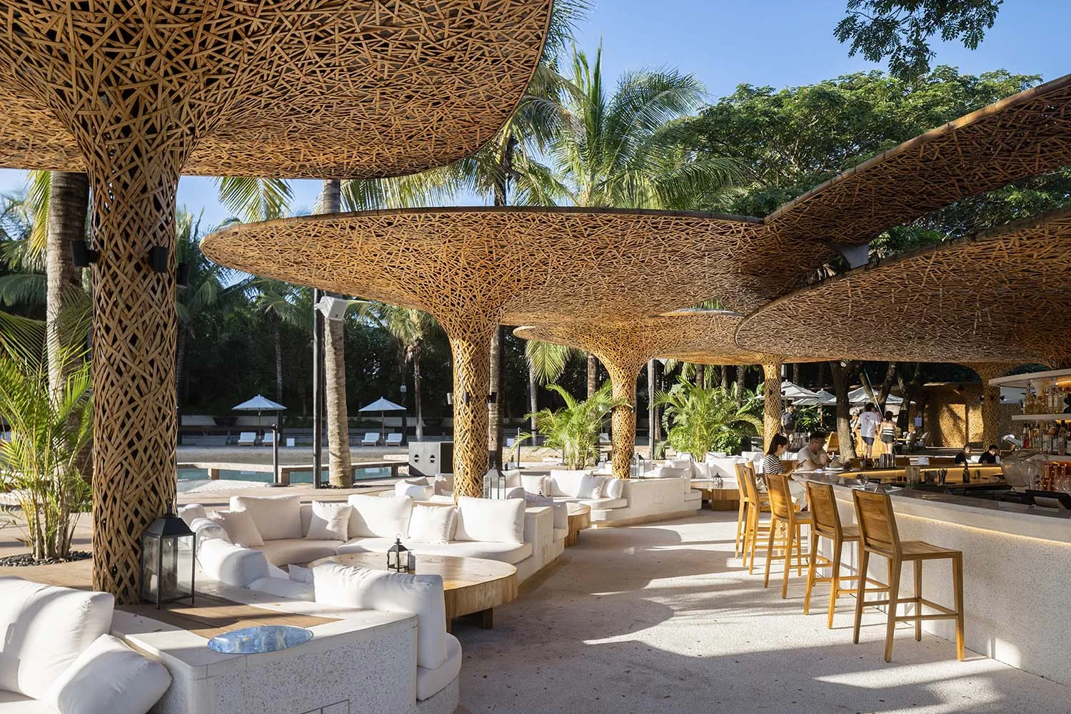 A relaxed outdoor dining space with several tables and chairs under large wooden umbrellas, surrounded by a warm and inviting atmosphere
