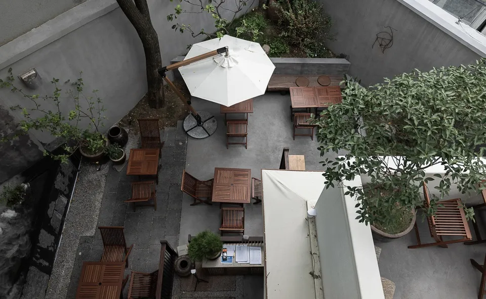 Outdoor dining area with multiple tables and chairs under a large umbrella, surrounded by a relaxed and inviting atmosphere
