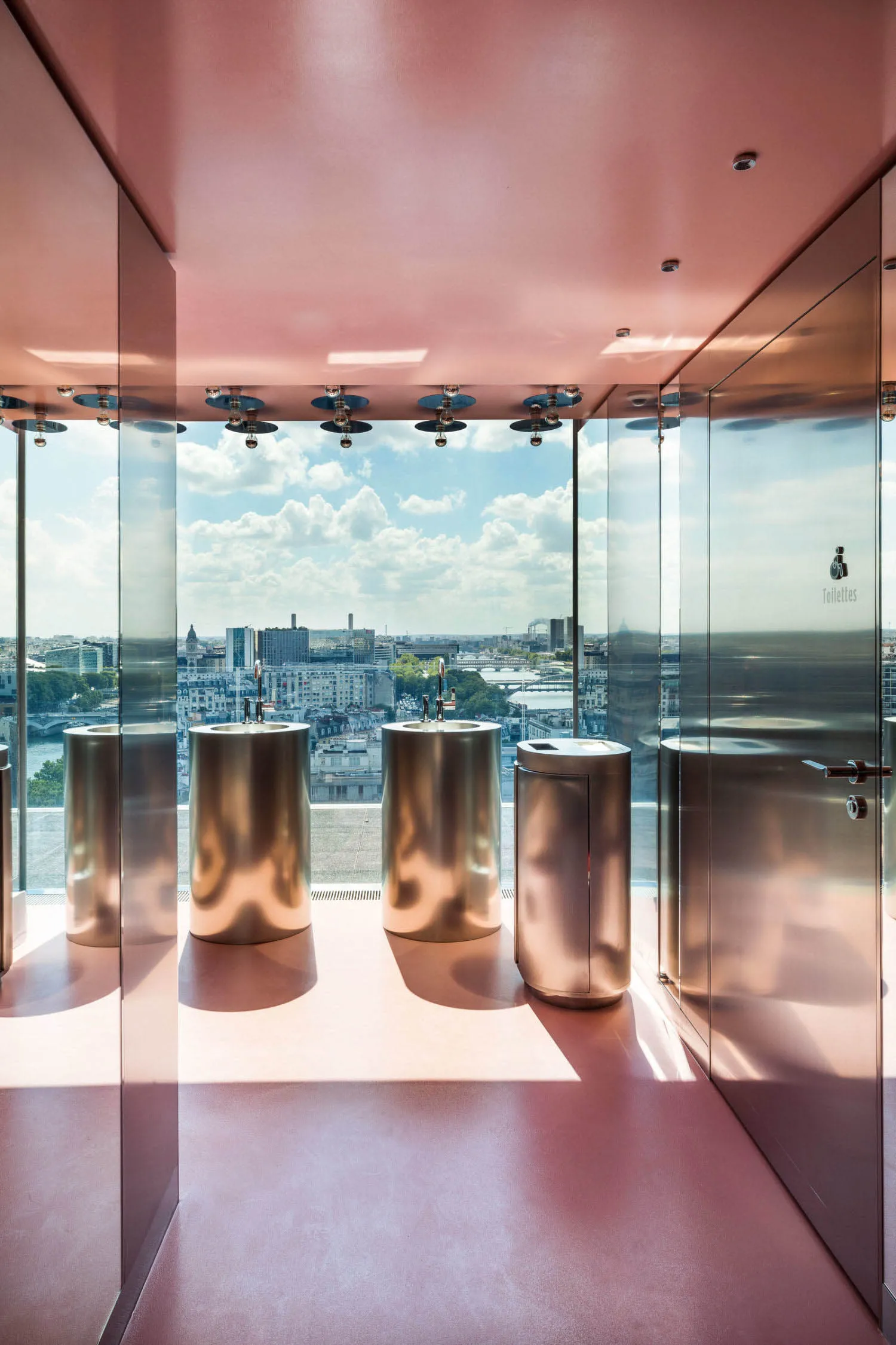 A modern bathroom with three metal sinks, a large window, and a bright and airy atmosphere