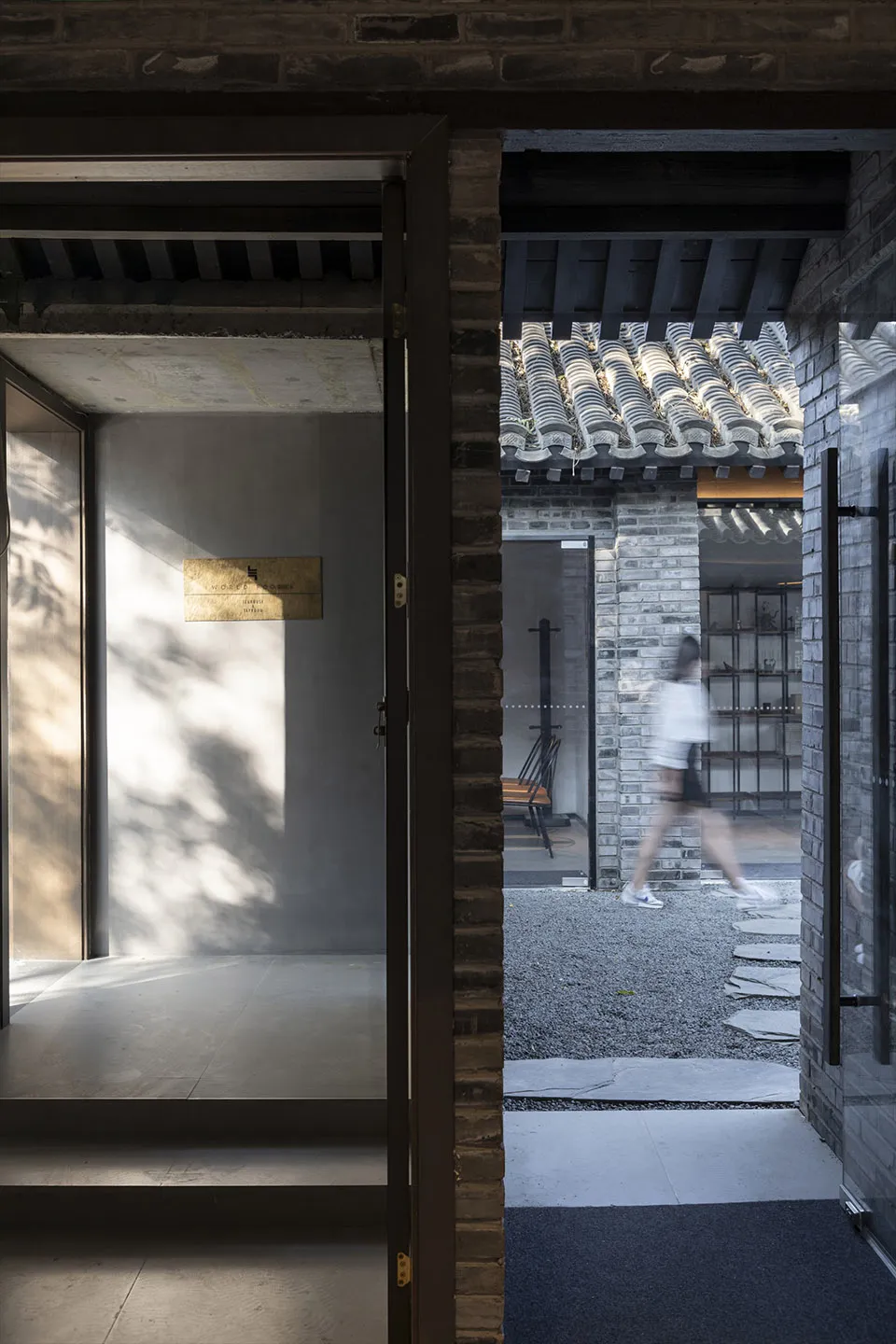 A traditional Asian building with open doors, a brick wall, and a tile roof, featuring a calm and serene atmosphere