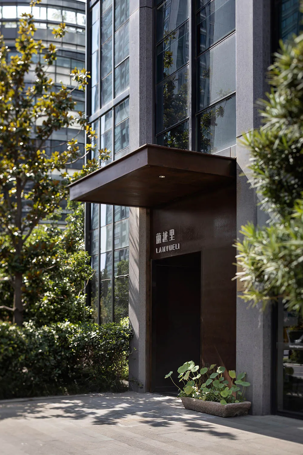 簡約亞洲建築，棕色門廊、盆栽植物，上方有窗戶，背景為混凝土牆面