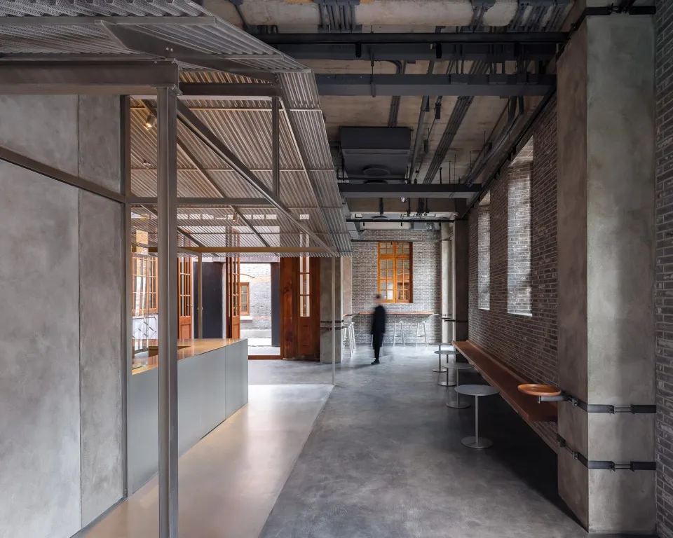 A spacious industrial-style hallway with concrete walls and floors, featuring multiple rooms and benches for seating