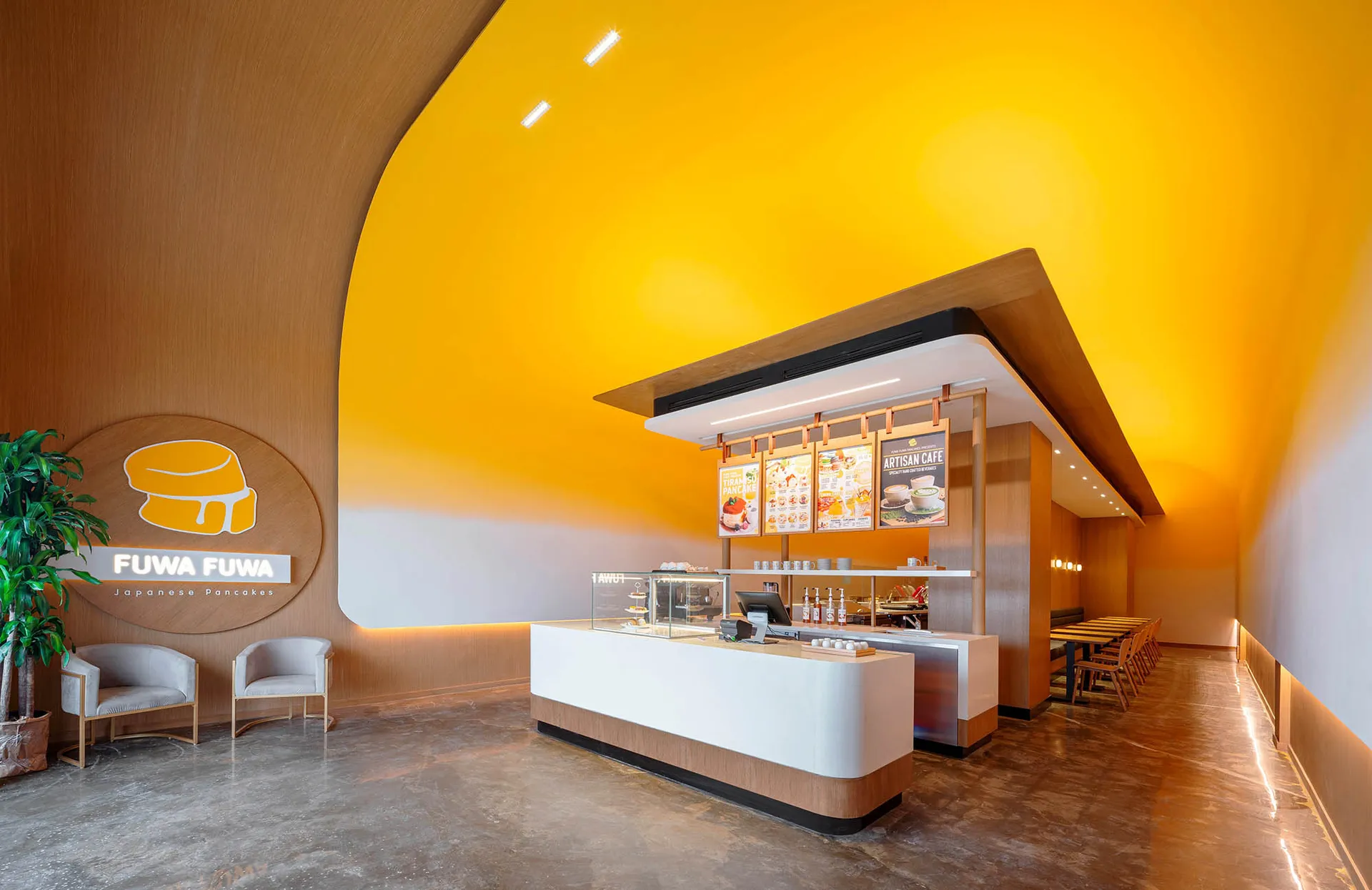A modern Japanese restaurant interior with a yellow theme, featuring a counter with a cash register and displayed food items, surrounded by cups and a bowl with a spoon