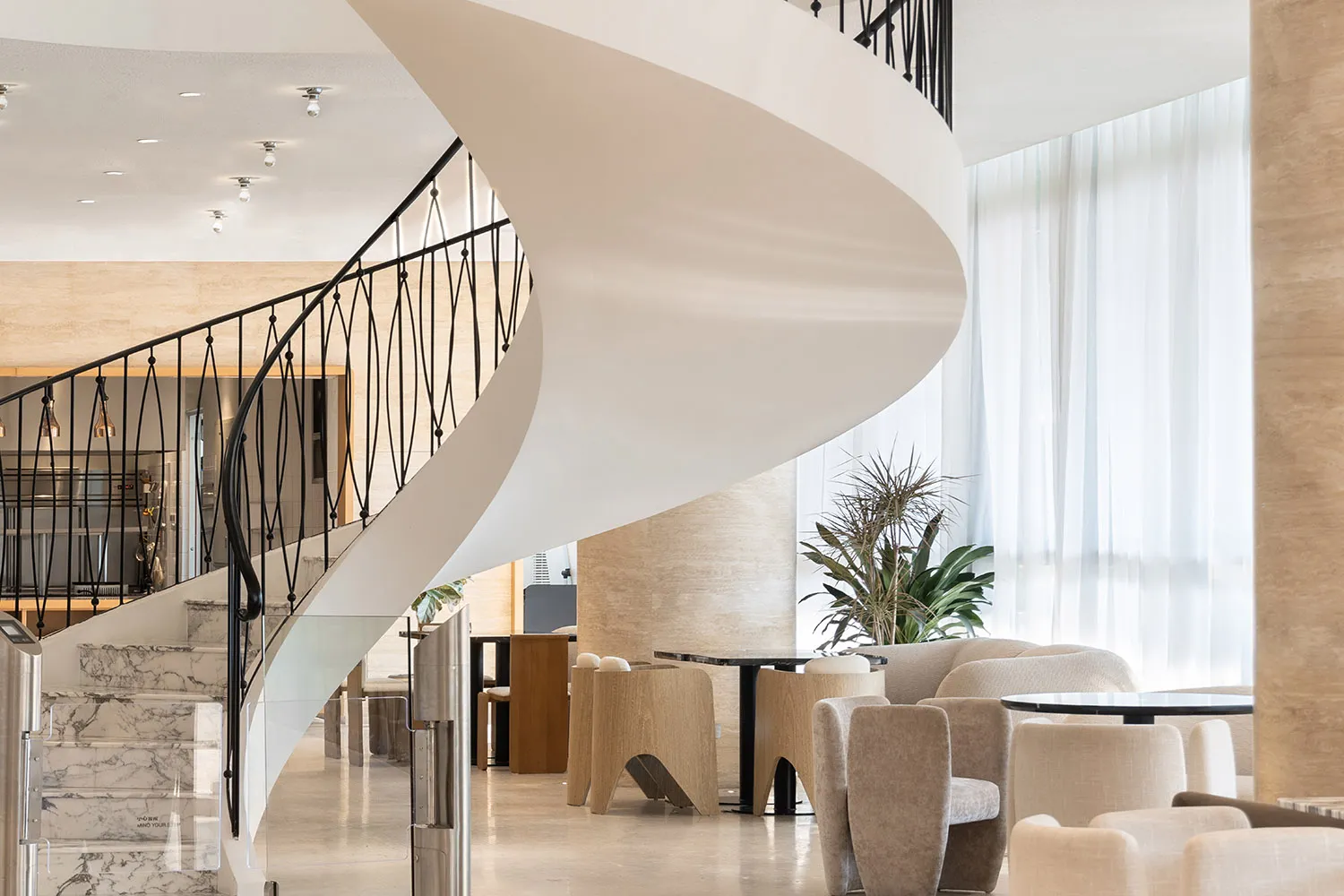 Elegant living space with a spiral wooden staircase, two couches, and a chair, featuring a sophisticated atmosphere and warm tones