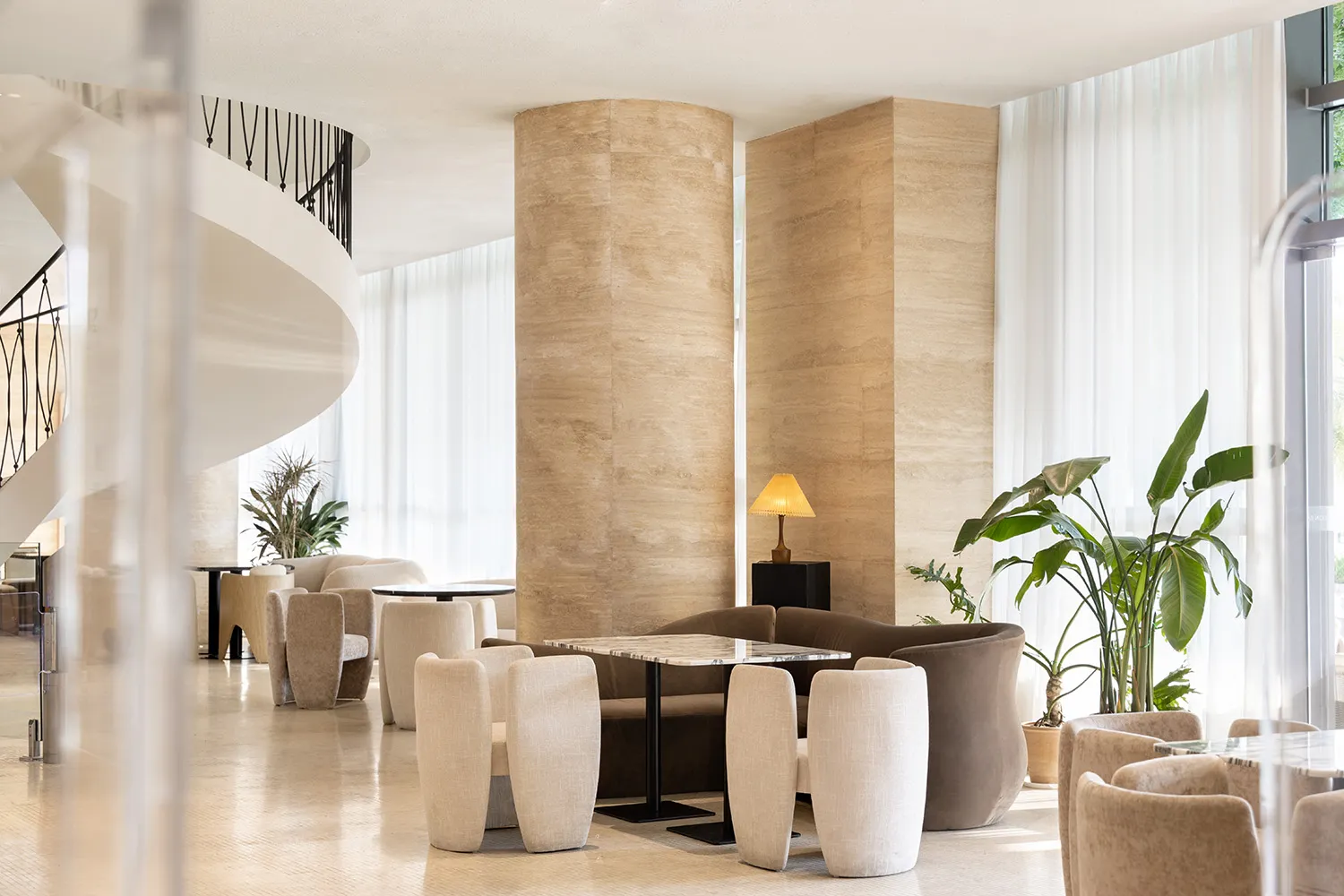 A modern living space with a large couch, chairs, and potted plants, featuring a well-lit and inviting atmosphere