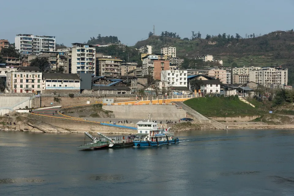 A bustling riverfront scene with a large boat and brick buildings, surrounded by people going about their daily activities