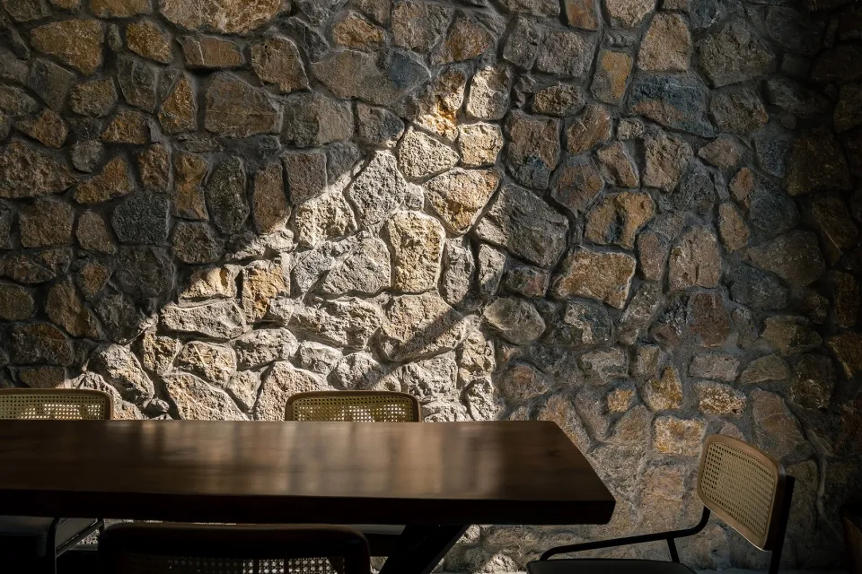 A warm and inviting dining area with a wooden table and chairs, surrounded by a stone wall and natural light