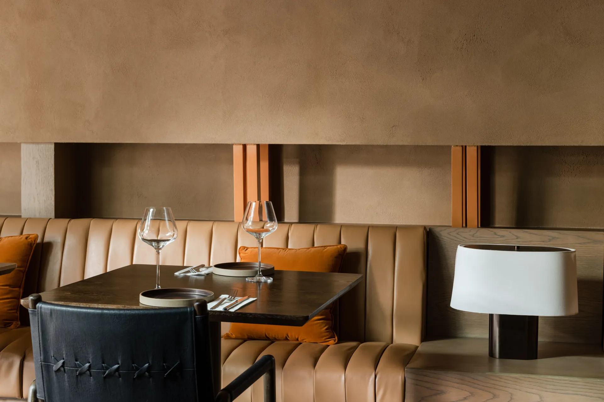Cozy restaurant interior with brown leather couches and chairs, dining tables, and wine glasses, set against warm brown and orange-toned walls