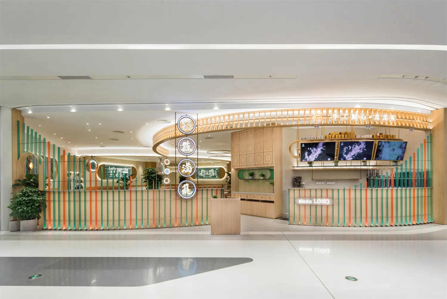 A warm and inviting hotel lobby with a wooden desk surrounded by potted plants and two TV screens on the wall
