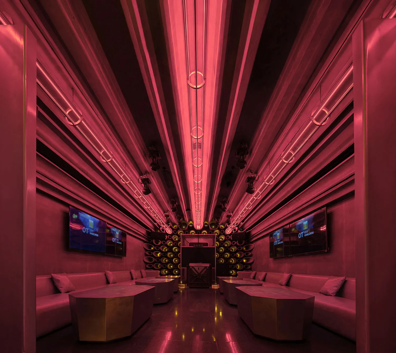 Modern living space with pink walls, ceiling lights, two couches, two chairs, and three TVs