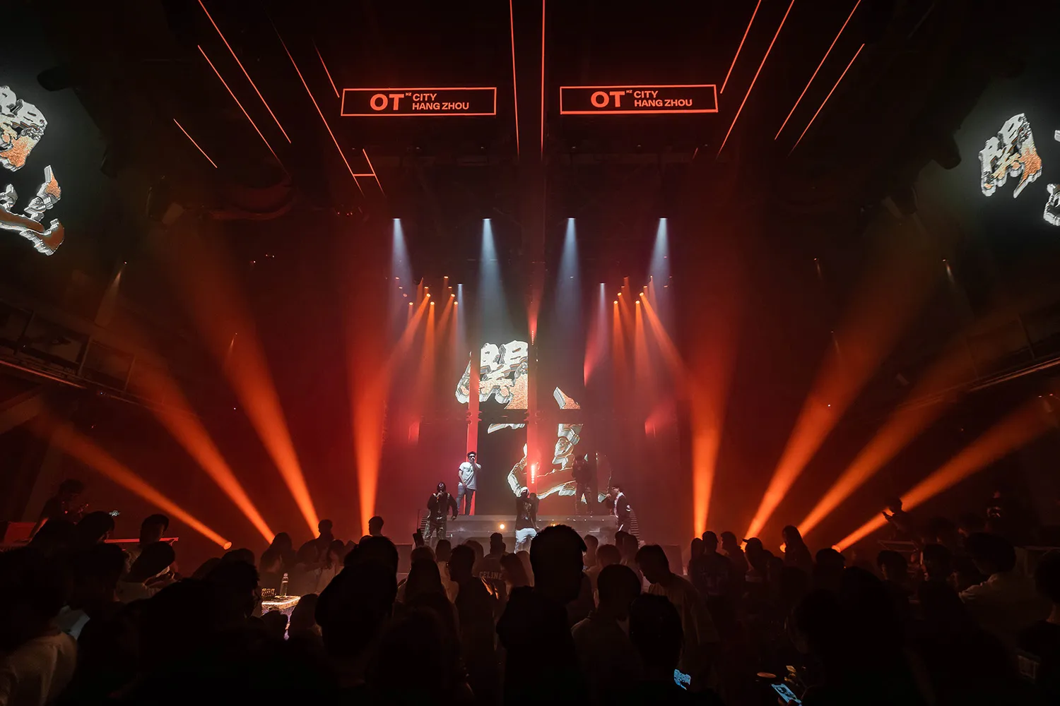 A lively indoor event venue with a stage and a crowd of people enjoying a performance, featuring a red brick wall and a mix of modern and traditional elements