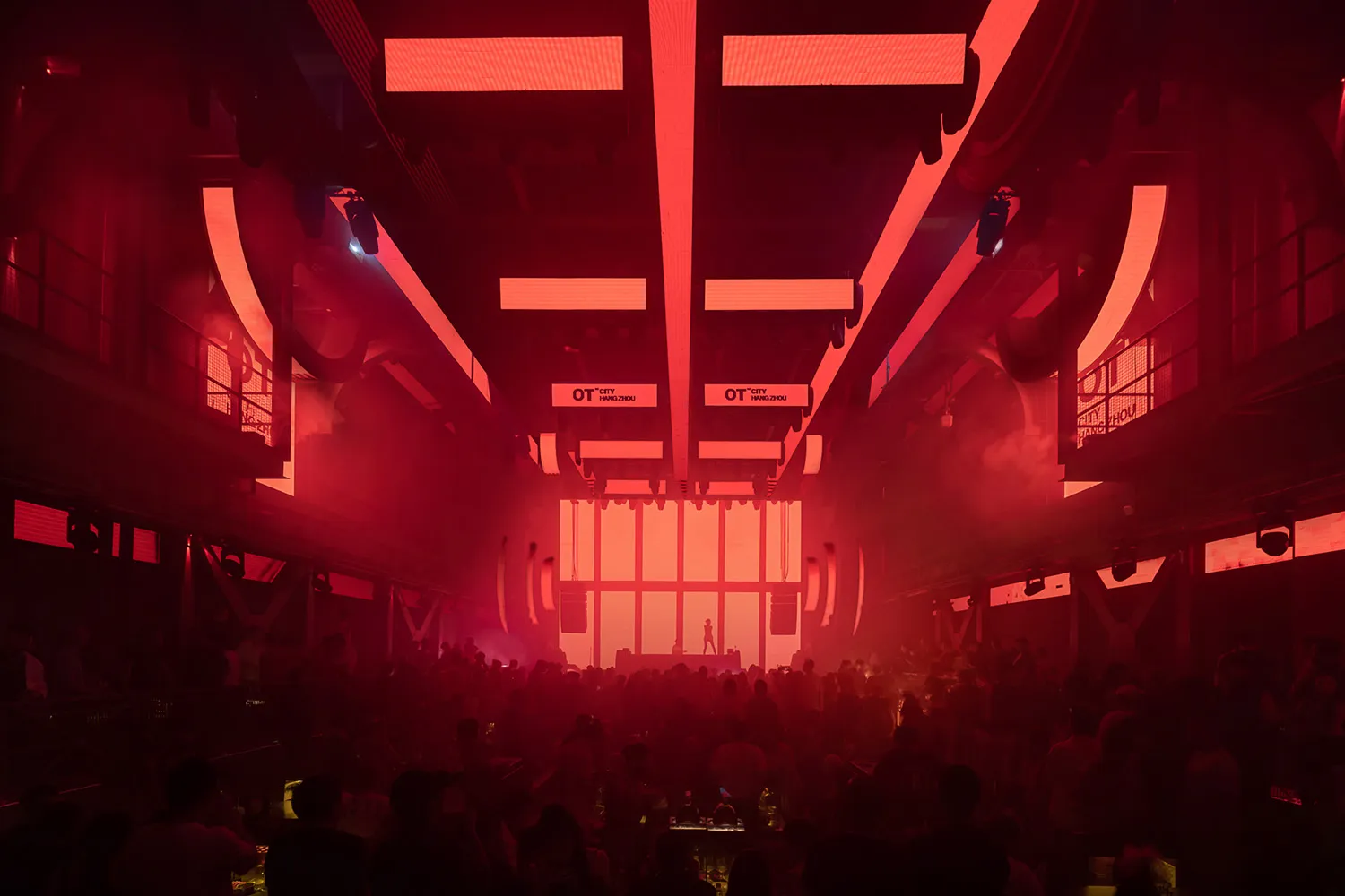 A crowded indoor event venue with a red glow, people standing and socializing, and scattered chairs