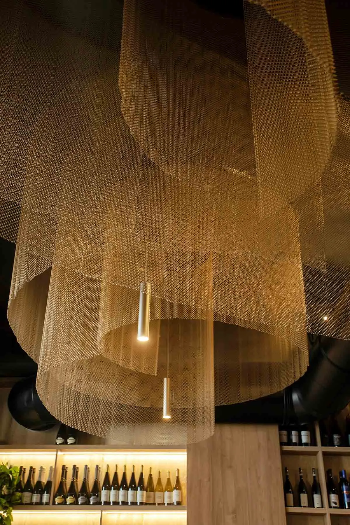 A dimly lit room with a minimalist aesthetic, featuring a large mesh ceiling fixture with suspended lights, creating a cozy atmosphere