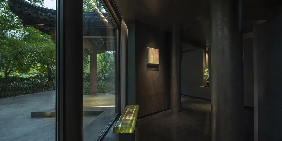 光線柔和的房間，窗邊有長椅、兩盆盆栽及展示畫作