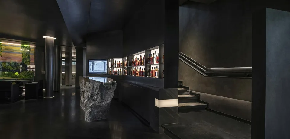 A sophisticated bar with a black and white theme, featuring stone and concrete elements, and bottles on shelves