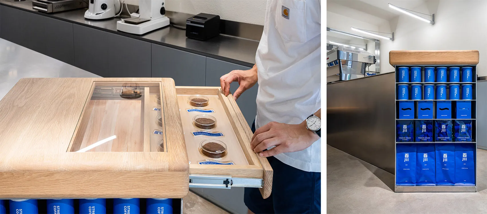 A man holds a wooden tray with small items in a kitchen or dining area with a countertop and multiple bottles in the background