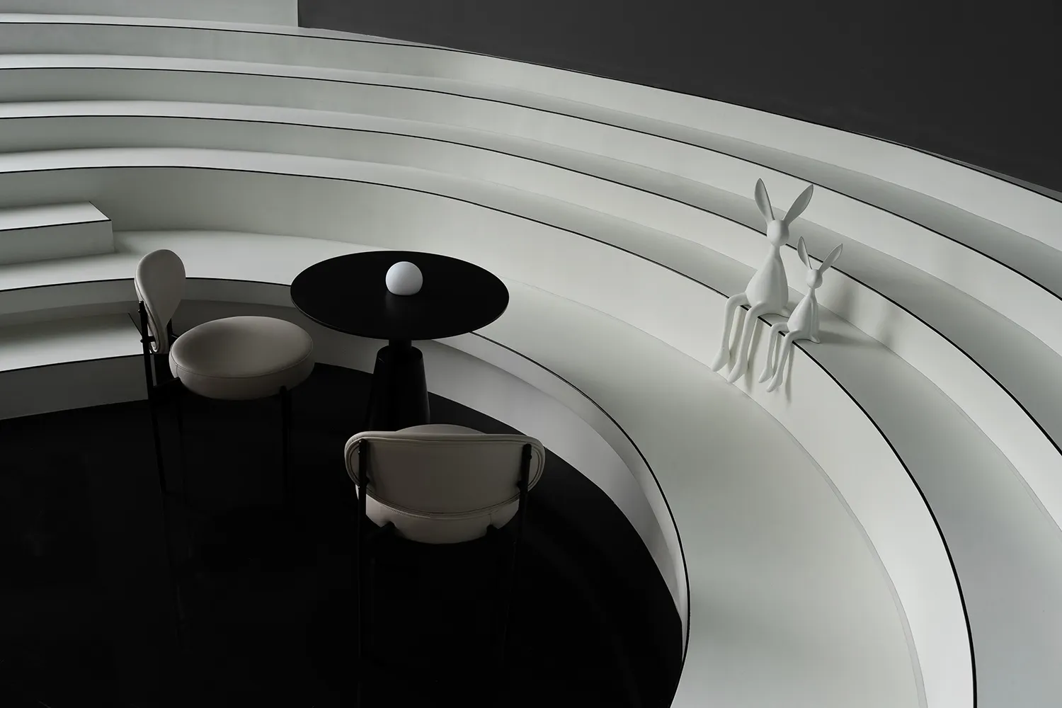 Modern living space with white walls, black floors, and a circular design featuring chairs, a dining table, and deer statues