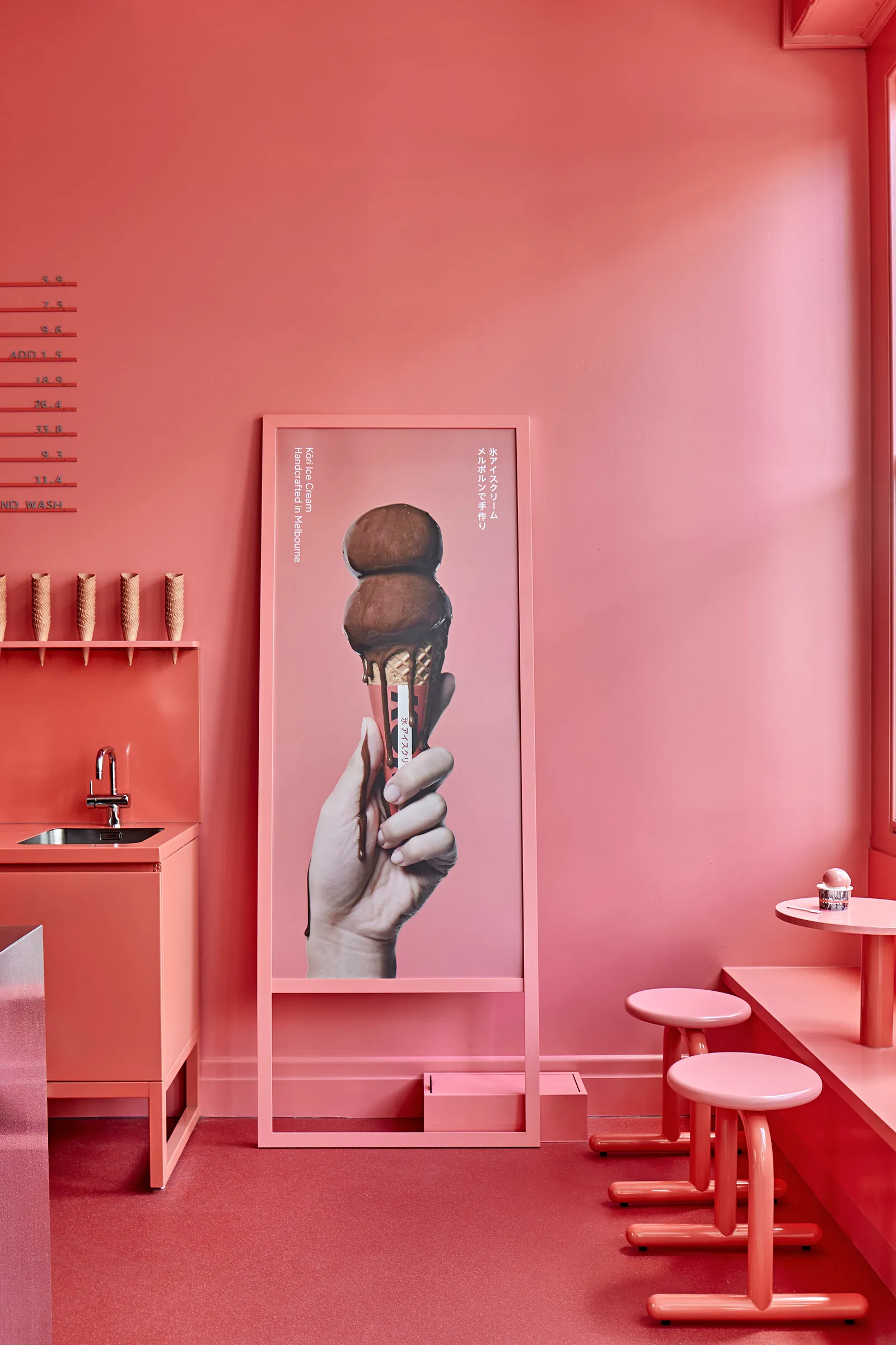A bright and cheerful room with a large pink wall featuring a fun ice cream poster, two chairs, and a sink, creating a playful atmosphere