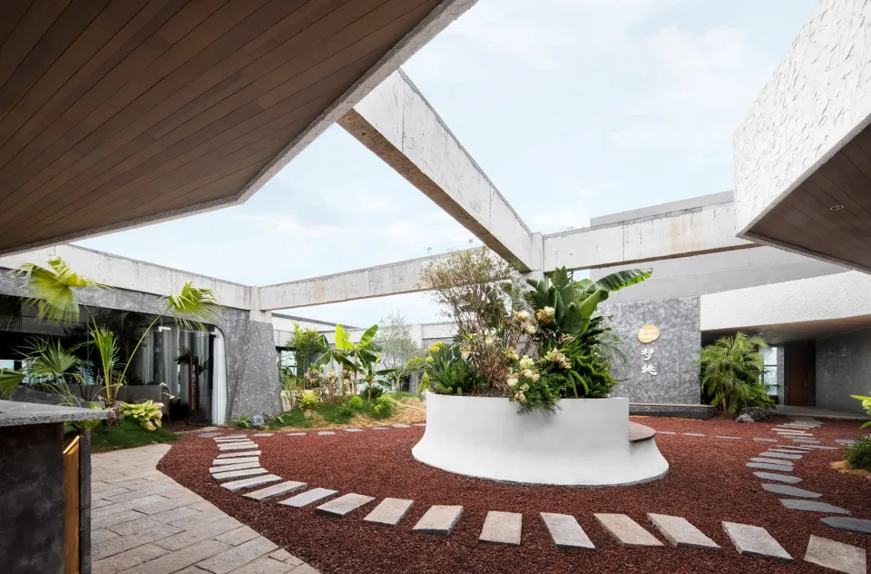 A serene and inviting outdoor space with a modern concrete building surrounded by plants and trees, featuring potted plants and a natural atmosphere