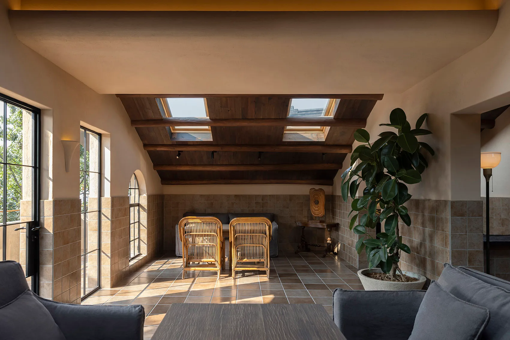 A warm and inviting living area with a dining table under a skylight, surrounded by chairs and a potted plant, with natural light filling the space