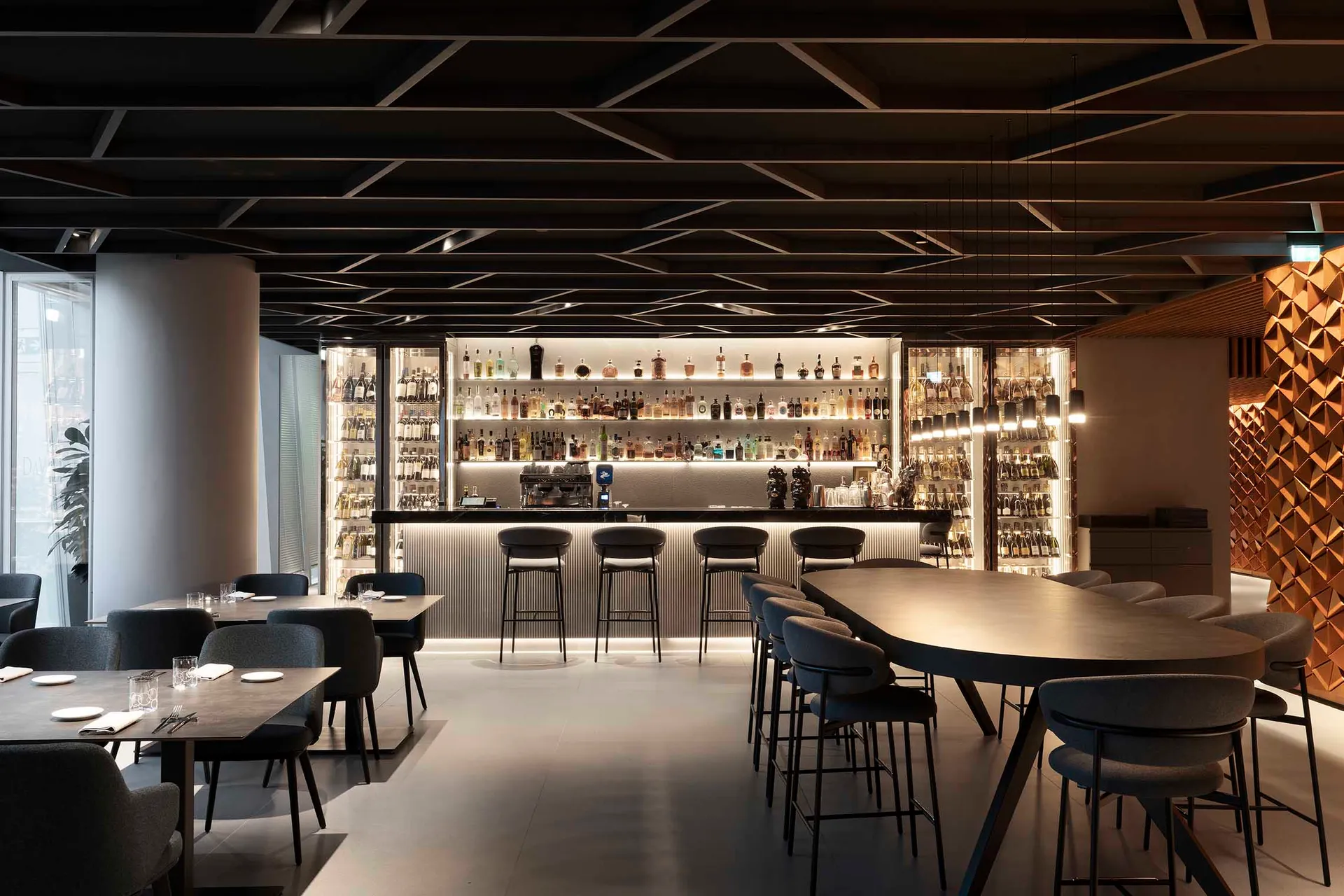 A modern bar area with a black and white color scheme, featuring a long counter and chairs, and a well-stocked counter with bottles