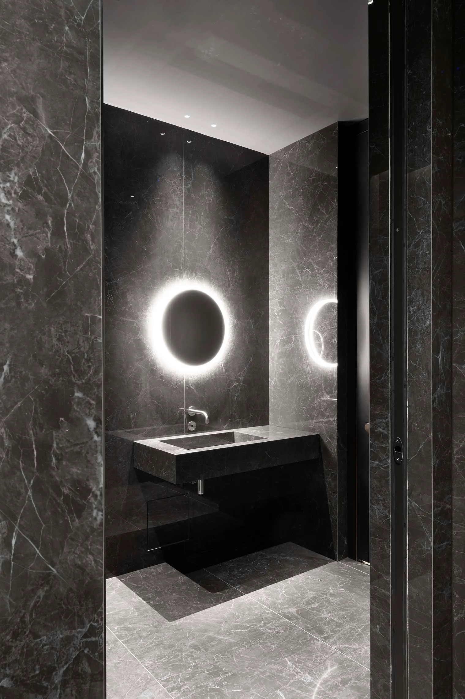 Modern bathroom with a sink, mirror, and shower area, featuring black marble flooring and sleek design