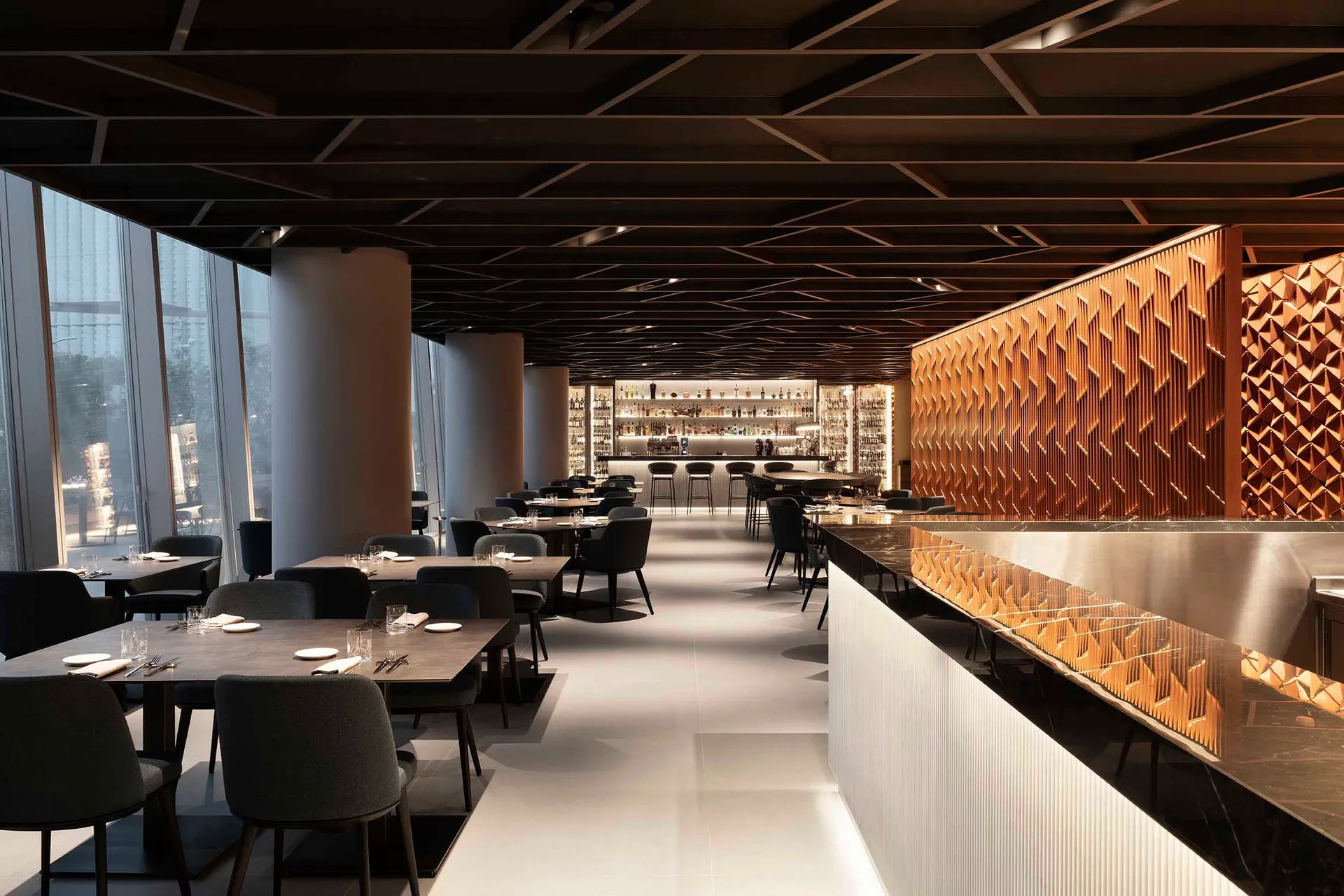 A modern restaurant interior with a long bar counter and dining tables, featuring sleek lines, contemporary elements, and warm inviting lighting